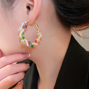 Detailed close-up of a gold hoop earring with colorful crystal beads and white pearls