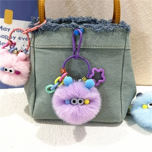 Cute plush monster keychain with colorful beads hanging on a denim bag strap