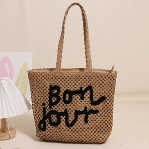 Straw woven tote bag with Bonjour embroidery shown in a warm indoor rustic aesthetic