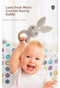 Detail of baby hand holding a gray crochet bunny rattle with a smooth wooden ring