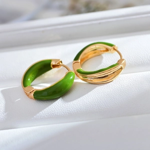 Close-up of golden geometric hoop earrings with green enamel coating on textured backdrop