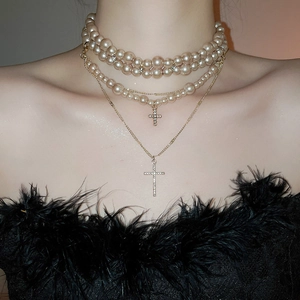 Detail view of a vintage multi-layer pearl necklace with rhinestone cross pendants on a model