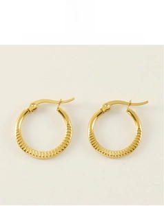 Close-up detail of golden hoop earrings featuring horizontal grooved textured patterns
