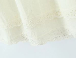Dettaglio di abito in cotone bianco con doppia balza e ricamo floreale traforato