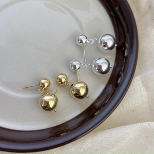 Dettaglio di orecchini a doppia sfera lucida in oro e argento su un piatto di ceramica