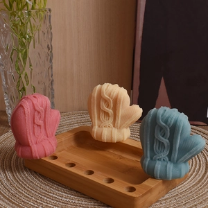 Three knitted wool mitten candles with intricate cable knit patterns in pastel colors