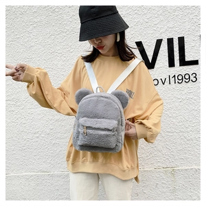 Detailed view of gray plush backpack with cute bear ears worn by model against a white wall