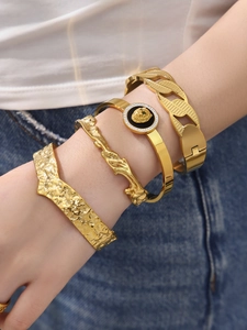 Detail of stacked gold stainless steel bracelets with lion head emblem and hammered texture