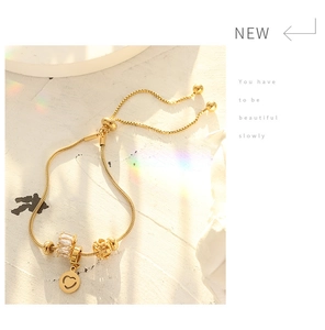Close-up of gold beaded bracelet with heart charm and rose details on marble background