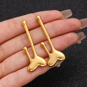 Macro shot of long gold heart earrings with polished finish held in a hand