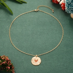 Collier doré avec pendentif cœur rouge sur fond vert foncé et décorations de Noël