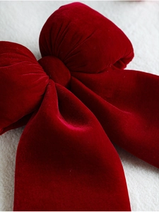 Close-up of a large red velvet Christmas bow decoration on a white textured background