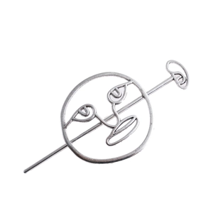 Detail view of a silver metal hair pin featuring a hollow abstract face design on white