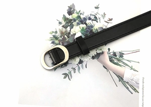 Detail of minimalist black faux leather belt with a light gold oval metal buckle