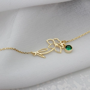 Detail of gold floral pendant with green zircon birthstone on white fabric background