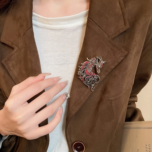 Detail of vintage hollow dragon brooch with red rhinestones on a brown suede coat