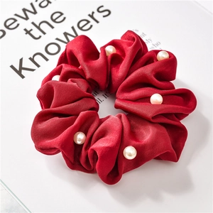Close-up of red silk scrunchie with elegant faux pearl beads and pleated fabric texture