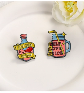 Detail of Self Love Potion and Juice enamel pins on white ceramic plate with flowers