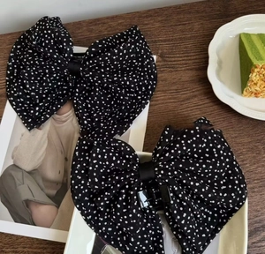 Gros plan de deux pinces à cheveux à nœuds en tulle noir à pois sur un décor en bois