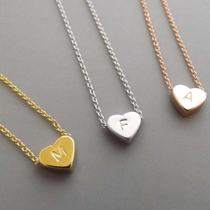 Close-up of stainless steel heart pendants with engraved initials in gold, silver, and rose gold.