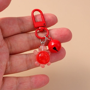 Macro view of red resin turtle keychain with matching metal bell and clasp detail