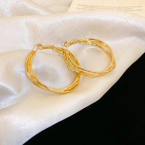 Detail of gold multi-layer twisted hoop earrings on white silk fabric background