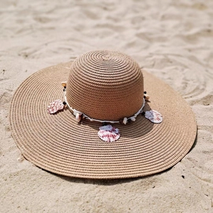 Detail of khaki straw sun hat with shell and wood bead trim on a sandy beach