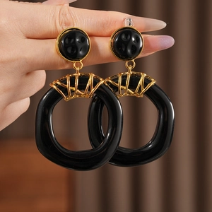 Gros plan de boucles d'oreilles géométriques en résine noire avec clous dorés en main