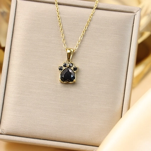 Détail du collier pendentif patte de chat dorée avec zircons noirs dans un coffret cadeau
