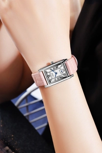 Detailed close-up of a square silver watch with pink leather strap and blue hands on wrist