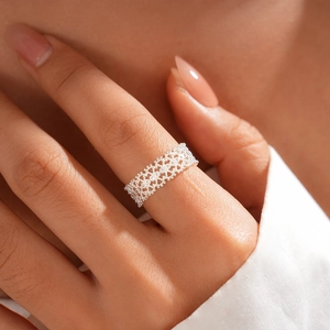 Close-up of a wide hollow lace flower open ring in silver finish on a female finger