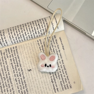 Detailed view of white plush bunny head charm with beige leather strap on open book