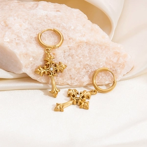 Detailed close-up of golden cross earrings with baroque patterns and white zircons