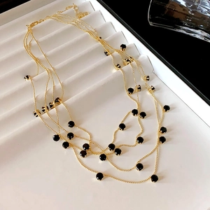 Vue détaillée d'un collier multi-rangs doré élégant orné de pierres noires rondes.