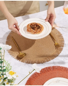 Dettaglio di tovagliette intrecciate rotonde con nappe su tavolo di marmo bianco