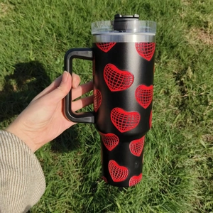 40oz black stainless steel tumbler with red disco heart patterns held outdoors over grass
