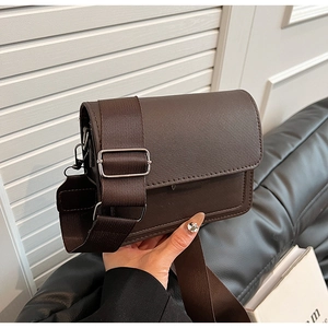 Detail of dark brown leather crossbody bag featuring wide nylon strap and silver buckle