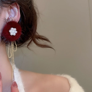 Detail of red pompom earrings with pearl flower and long golden tassel on a model