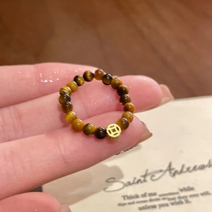 Macro detail of tiger eye beaded ring with a gold coin charm held by fingers