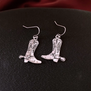 Macro shot of silver vintage cowboy boot earrings with floral engraving and spur details