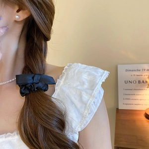 Detail of a black satin bow scrunchie on a ponytail with elegant cream lace clothing