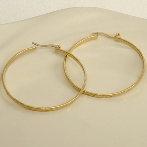 Detailed view of large gold hoop earrings featuring geometric embossed textures on a tray