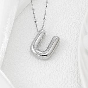 Macro shot of silver balloon letter U pendant on a ball chain over white silk