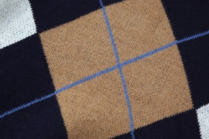 Macro shot of navy blue and beige argyle knit pattern with crisscross stitch detail