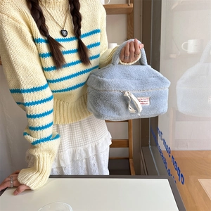 Large capacity light blue plush makeup bag for travel storage held by a model in a cafe