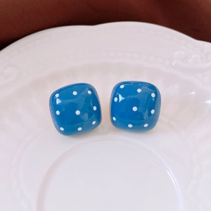 Macro shot of blue square stud earrings with white polka dots on a white relief plate