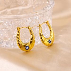 Gold U-shaped Evil Eye earrings with ribbed texture hanging on a crystal glass bowl
