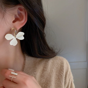 Boucles d'oreilles fleurs blanches asymétriques avec clous dorés portées par un modèle