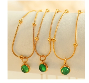 Detail of three golden snake chain bracelets with green gemstone pendants on display
