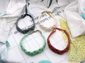 Detail of four handmade braided cotton elastic headbands in grey, beige, green and red